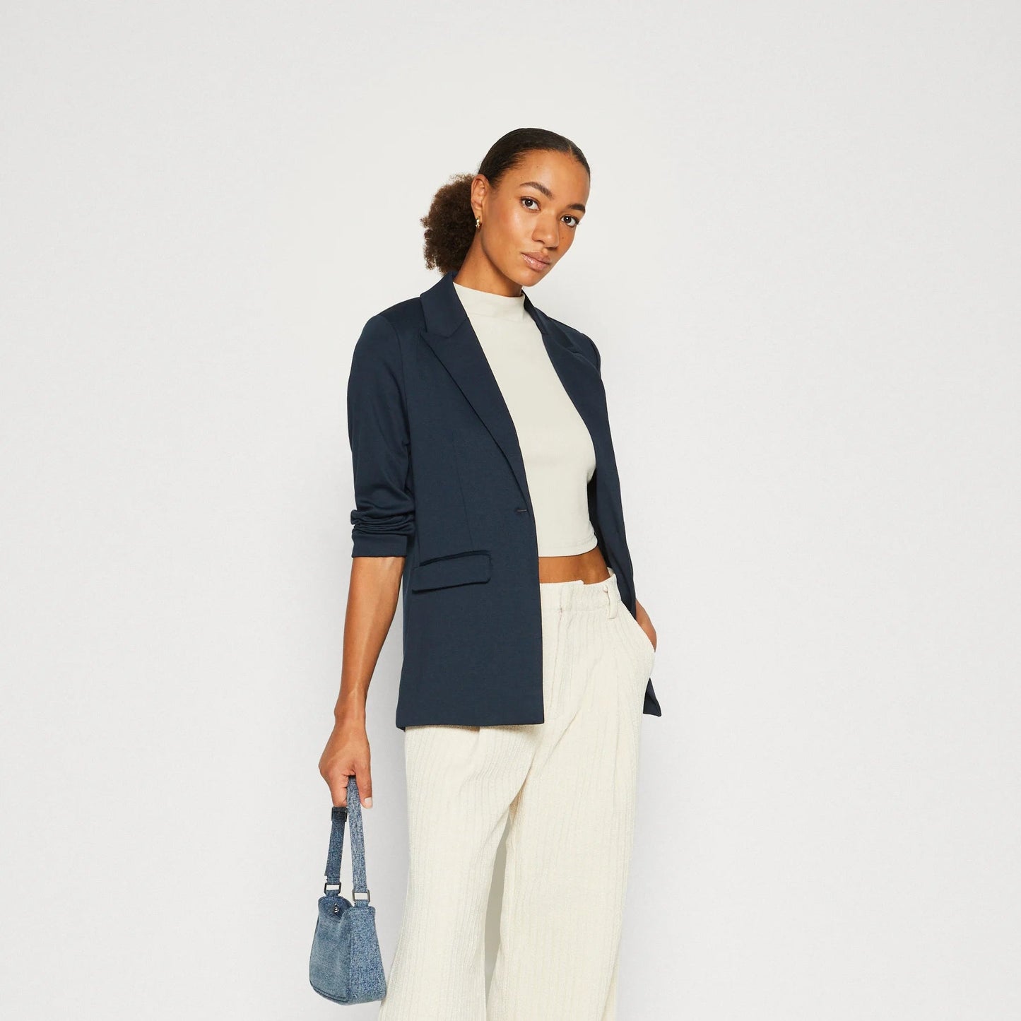 Woman wearing a navy blazer, white top, and wide-leg pants on a white background