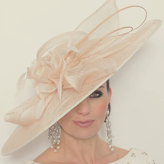 Woman wearing a large, decorative beige hat with a bow, against a plain background.
