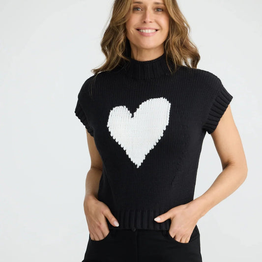 Woman wearing a black sweater with a white heart design on a plain background
