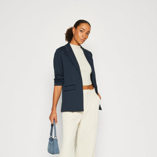 Woman wearing a navy blazer, white top, and wide-leg pants on a white background